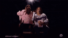 a woman and a little girl are sitting in a theater eating popcorn and drinking soda