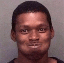 a man in a black shirt is smiling for the camera in a mugshot .