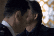 two men in suits are kissing in front of a window