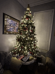 a christmas tree in a living room with a picture on the wall above it