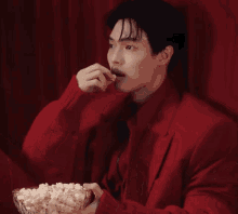 a man in a red jacket eating popcorn from a bowl