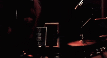 a man is playing drums in a dark room while holding a drum stick .
