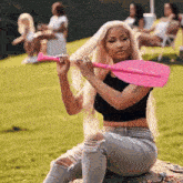 a woman is holding a pink paddle in her hand while sitting on the grass .