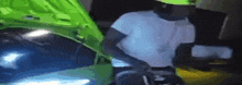 a man in a white shirt is standing next to a green car with the hood open .