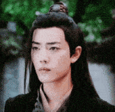 a young man with long hair and a ponytail looks to the side
