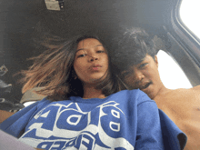 a boy and a girl are sitting in a car and the girl is wearing a blue shirt that says " aoe "