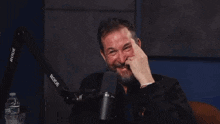 a man with a beard is laughing while sitting in front of a rode microphone .