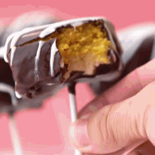 a close up of a person holding a chocolate cake pop with a bite taken out of it
