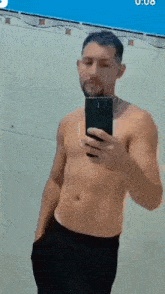a shirtless man is taking a selfie in a bathroom with his phone .