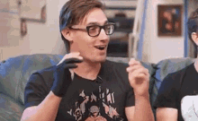 a man wearing glasses and gloves is sitting on a couch talking to another man .