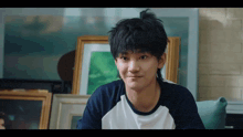 a young man in a blue and white shirt is sitting in front of framed pictures