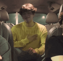 a man in a yellow sweater is sitting in the back of a car