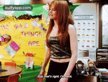 a woman in a crop top is standing in front of a bulletin board that says `` he who things are '' .