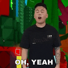 a man in a black t-shirt is standing in front of a colorful background and says yeah .