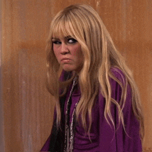 a woman with blonde hair is wearing a purple top
