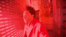 a man in a red jacket is standing in a dark room with a red light behind him .