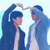two men are standing next to each other and making a heart shape with their hands .