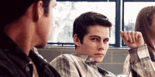 a young man in a plaid shirt is sitting in a classroom talking to another young man .