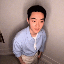 a young man in a light blue shirt and khaki pants is standing in a corner of a room .
