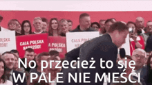 a man in a suit stands in front of a crowd holding a sign that says cala polska