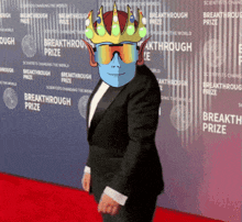 a man wearing a crown and sunglasses stands in front of a wall that says " breakthrough prize "