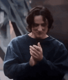 a man in a blue sweater is clapping his hands together in a close up .