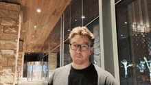 a man wearing glasses is standing in front of a large window