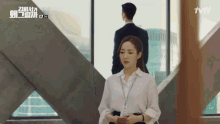 a woman in a white shirt stands in front of a window with a tvn logo on the bottom