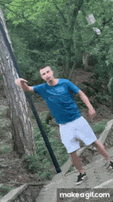 a man in a blue shirt and white shorts is standing next to a tree in the woods