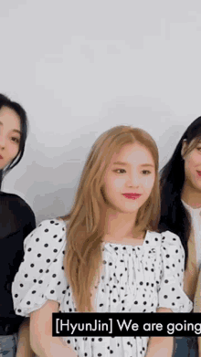 a girl in a white polka dot dress is standing next to two other girls and says hyunjin we are going