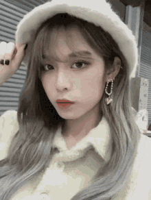 a woman wearing a white hat and earrings is taking a selfie