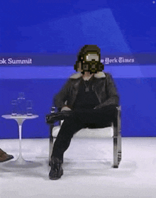 a man wearing a gas mask is sitting in a chair at a conference .