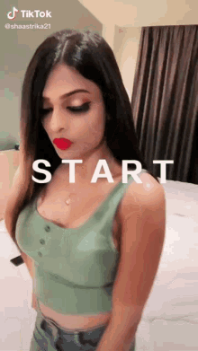 a woman in a green tank top is standing in front of the word start