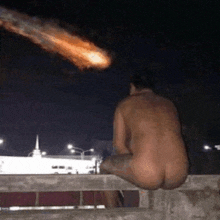a naked man is sitting on a balcony looking at a comet .