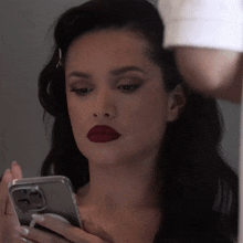 a woman with red lipstick is looking at her cell phone