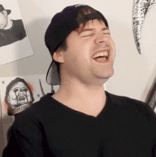 a man wearing a hat and a black shirt is laughing in front of a poster that says " diverse "