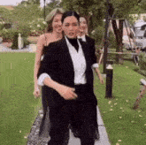 a woman in a tuxedo is walking down a sidewalk with other women .