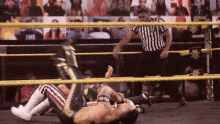 two men are wrestling in a wrestling ring while a referee looks on .
