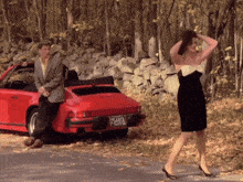 a woman in a black and white dress stands in front of a red porsche with a license plate that says 28411