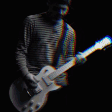 a man in a striped shirt playing a guitar in a dark room