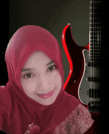 a woman wearing a red hijab is smiling in front of a red guitar
