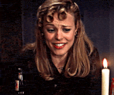 a woman is smiling in front of a lit candle and a bottle of beer