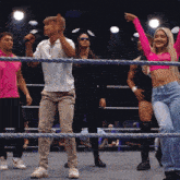 a group of people are standing in a wrestling ring one of them is wearing a pink shirt