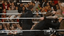 a group of men are wrestling in a wrestling ring with a crowd behind them .