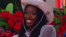 a woman wearing a white cowboy hat is laughing with her mouth open in front of red roses .