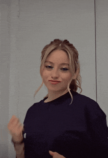 a woman in a black shirt is making a funny face while standing in front of a white wall