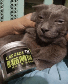 a person is holding a cat next to a can of cat zaza