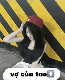 a girl wearing a red hat is sitting in front of a yellow and black striped wall with a white arrow pointing up