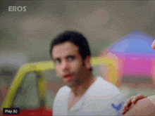 a man in a white shirt is standing in front of a yellow car with eros written on the bottom