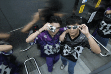 a man taking a picture of another man in an elevator with a sign that says ' emergency exit '